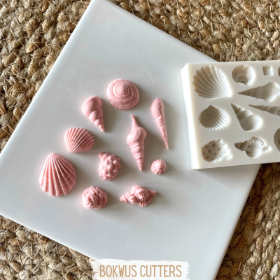 Molde de silicone com cavidades em forma de conchas, conchas cor-de-rosa feitas, superfície branca e tecido castanho trançado