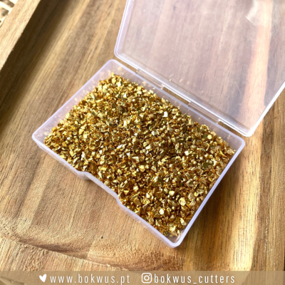 Caixa transparente com pequenos pedaços dourados brilhantes sobre madeira