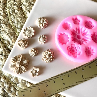 Forma de silicone rosa com cavidades de flores, peças decorativas creme, régua e superfície branca sobre tecido natural.