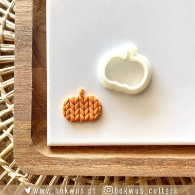 Cortador e decoração de massa em forma de abóbora em branco e laranja sobre bandeja de madeira em fundo claro