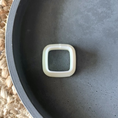 Anel quadrado translúcido sobre prato preto texturizado.