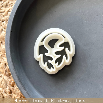 Cortador de biscoitos branco em forma de folha numa travessa cinza sobre tapete de fibras naturais