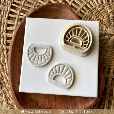 Três cortadores semicirculares de massa brancos com padrões de gomos, sobre placa branca e base de madeira em fibra trançada.