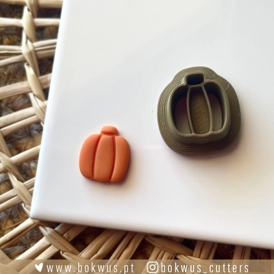 Cortador de biscoitos em forma de abóbora e abóbora modelada laranja sobre superfície branca e fundo de madeira