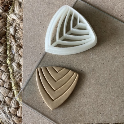 Dois moldes triangulares com padrão de linhas em V, um branco de plástico e outro castanho, sobre pedra e tapete trançado