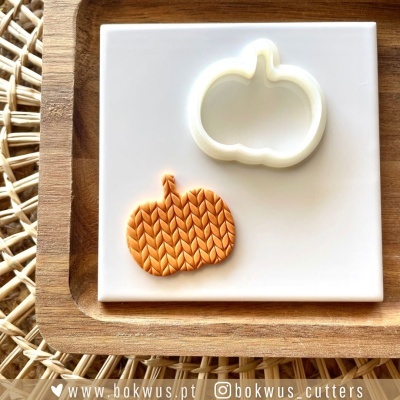 Cortador de biscoitos em forma de abóbora e pasta laranja com padrão trançado sobre prato branco e base de madeira