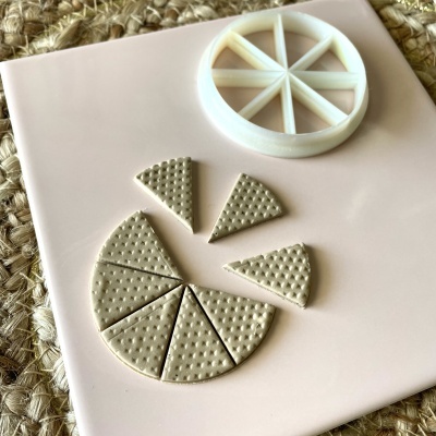 Molde branco redondo com divisões e pedaços triangulares texturizados sobre placa rosa