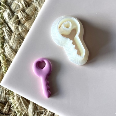 Cortadores de biscoitos em forma de chave branco e rosa sobre superfície rosa claro com tapete trançado