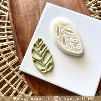 Dois cortadores de biscoitos em forma de folhas com detalhes, em fundo branco e madeira