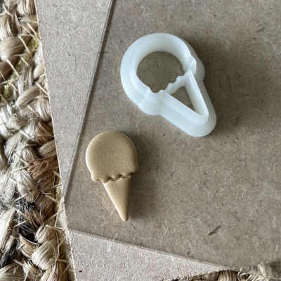 Molde branco e peça dourada em forma de gelado sobre papel castanho e tecido trançado.