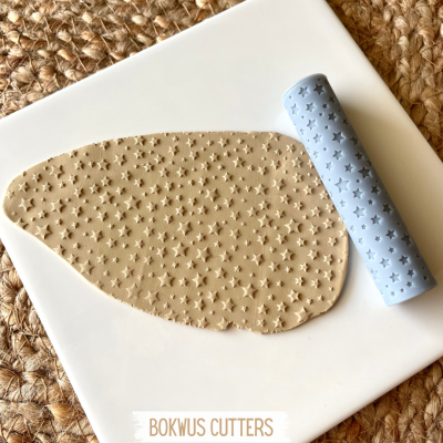 Rolo de massa azul claro com padrão de estrelas e massa estampada em superfície branca