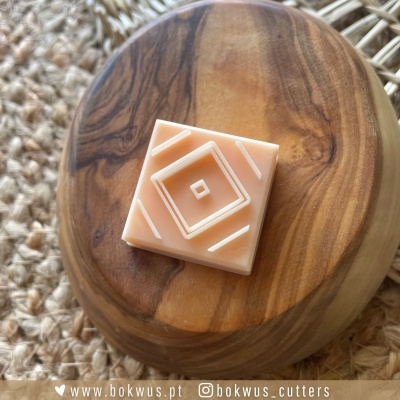 Cortador de biscoitos quadrado com padrão geométrico em relevo sobre base de madeira redonda