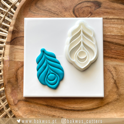 Cortador de massa em forma de pena branco e impressão azul sobre placa branca numa tábua de madeira