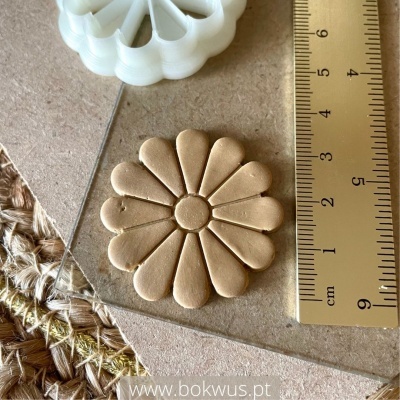 Dois moldes de flores, branco em plástico e bege em couro, com régua de 9 cm ao lado sobre superfície de tecido e papel.