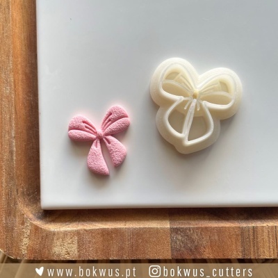 Dois cortadores de massa em forma de laço, um rosa e outro branco, sobre tábua de madeira