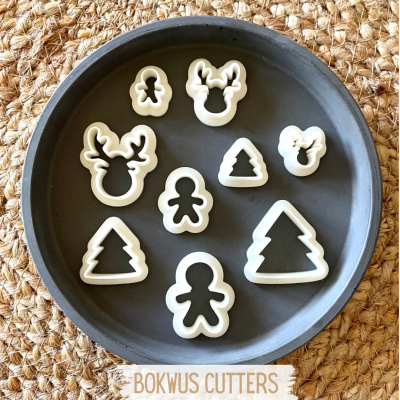 Cortadores de biscoitos natalícios em travessa cinza sobre tecido de palha