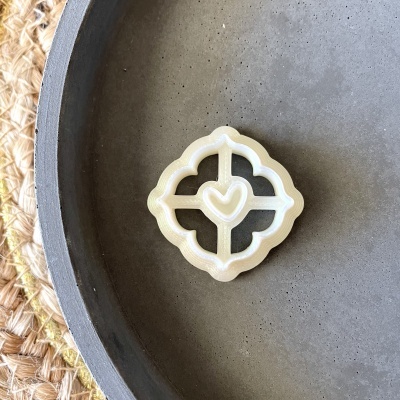 Selo plástico branco translúcido com desenho de coração no centro, sobre prato cinza e tapete de palha