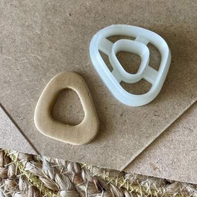 duas pegas triangulares, uma branca de plástico e outra bege de espuma, sobre papelão e tecido rústico.