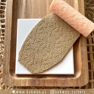 Rolo de textura laranja com padrão floral e massa estampada sobre bandeja de madeira