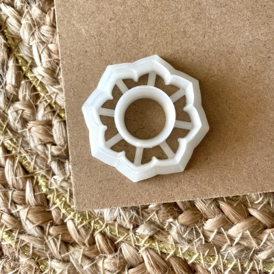Peça plástica branca decorativa em forma floral sobre cartão e tapete de fibras naturais