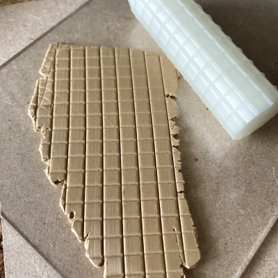 Massa bege quadriculada com rolo de textura branco numa superfície de azulejo cinza