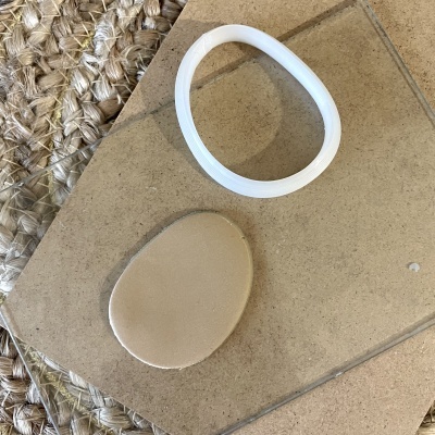 Pulseira branca elástica e suporte de espuma bege oval sobre pedra clara e tapete trançado