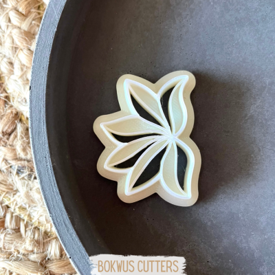 Cortador de biscoitos em forma de folha branco numa superfície preta rodeada por tapete de fibra natural