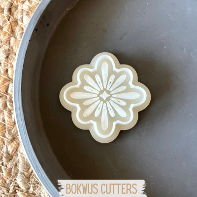 Cortador de massa branco com padrão floral em relevo dentro de prato cinza