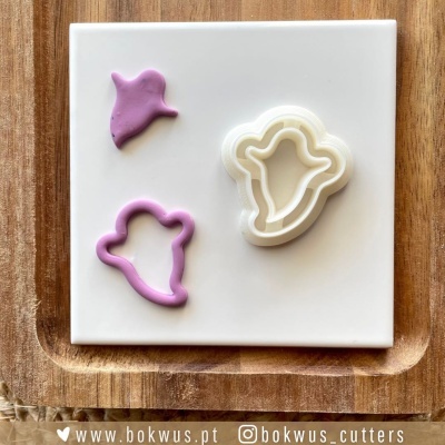 Cortadores de fantasma de plástico branco com massa rosa em forma de fantasma sobre placa branca e base de madeira