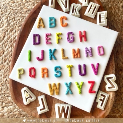 Letras coloridas do alfabeto sobre placa branca e tábua de madeira com fundo de tecido trançado