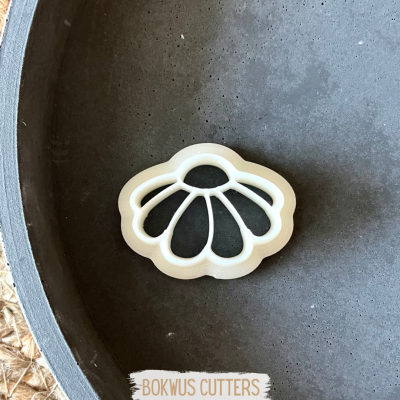 Cortador de bolachas em formato de flor branca numa superfície cinzenta.