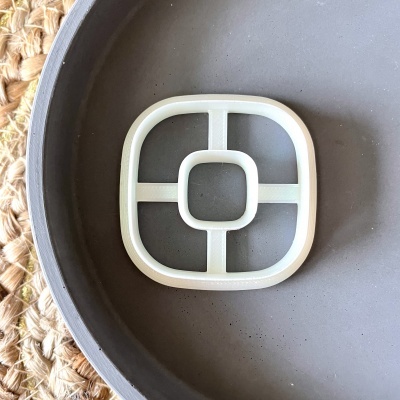 Peça plástica branca quadrada arredondada num prato cinza de cerâmica