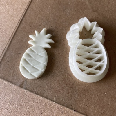 Duas peças de plástico branco em forma de ananás, carimbo e impressão sobre cartão castanho