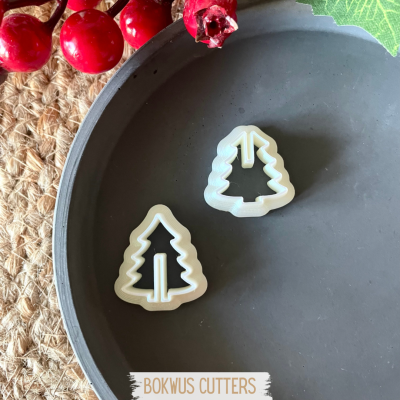 Dois cortadores de biscoitos em forma de árvore de Natal brancos numa bandeja cinza com bagas vermelhas decorativas