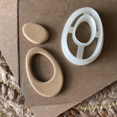 Moldes em plástico branco e forma de silicone bege com recortes ovais sobre cartão e tapete de fibra