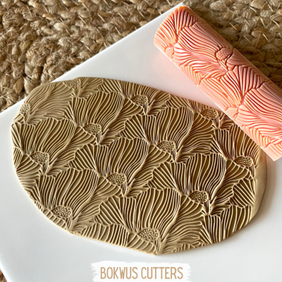 Placa oval com padrão floral gravado e rolo de textura cor de salmão em fundo branco.