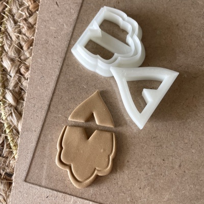 Cortadores de biscoitos em plástico branco com massa em forma de folha e triângulo em fundo de cartão