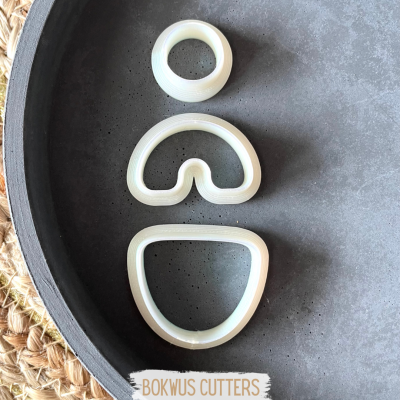 Três cortadores de massa brancos em formas geométricas sobre prato cinza com etiqueta BOKWUS CUTTERS