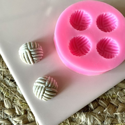 Molde de silicone rosa com cavidades redondas e objetos redondos cinza texturizados