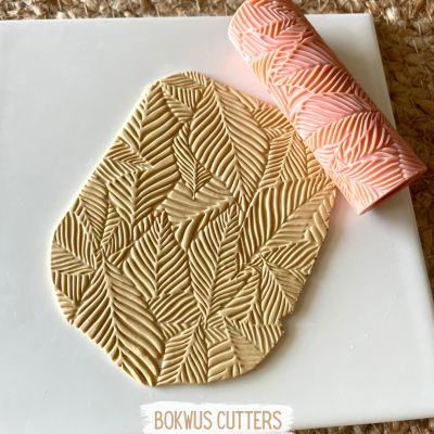 Rolo de textura rosa com padrão de folhas sobre massa bege com padrão igual