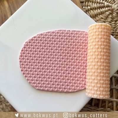 Placa branca com massa rosa texturizada com corações e rolo texturizador bege com padrão de corações