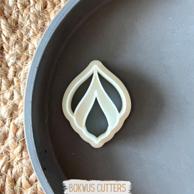 Cortador de bolachas branco em formato de folha num prato cinzento sobre juta