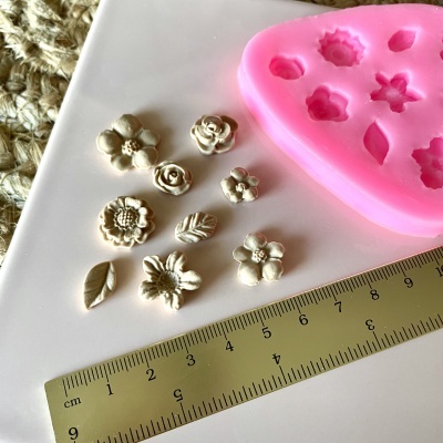 Molde de silicone rosa com formas de flores e folhas brancas e régua dourada em superfície branca