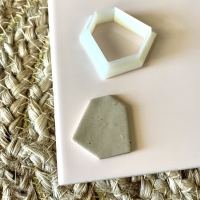 Forma pentagonal branca de plástico e peça pentagonal de cerâmica cinzenta sobre superfície branca