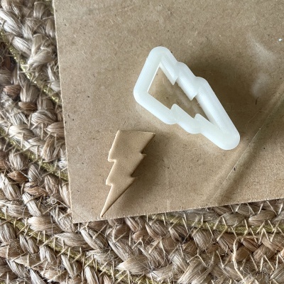 Cortante de plástico branco em forma de raio com massa marrom com a mesma forma sobre cartão e tapete tecido