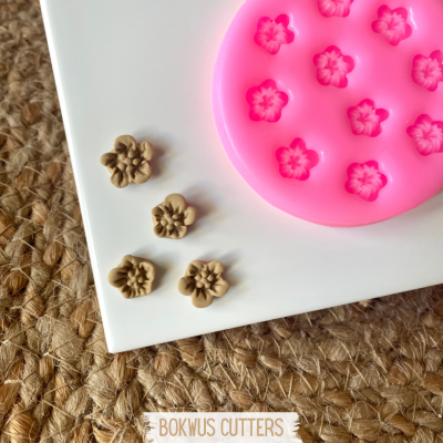 Molde de silicone rosa com formas de flores pequenas e flores de barro castanho claro feitas no molde sobre fundo branco e superfície rústica