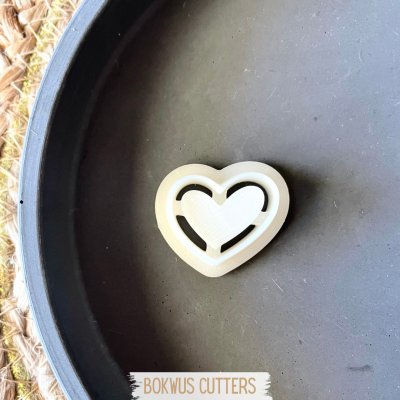 Cortador de bolachas de coração branco numa superfície escura com tapete de fibras ao fundo