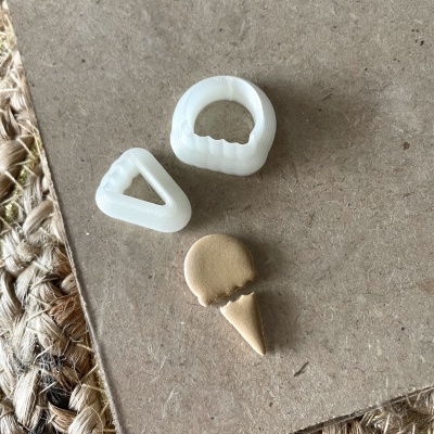 Três objetos pequenos em plástico branco e bege sobre superfície castanha e tapete de fibras naturais.