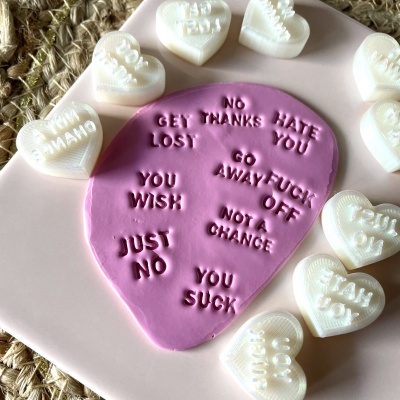 Objetos em formato de guitarra rosa com frases em relevo e corações brancos com textos