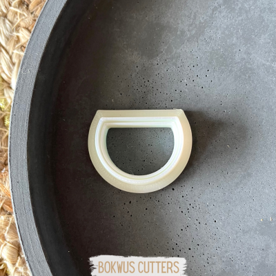 Cortante semi-circular branco em bandeja cinza escura com fundo de ráfia clara.